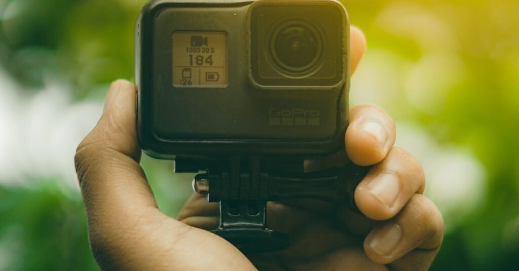 Close-up of a hand holding an action camera against a green leafy background.