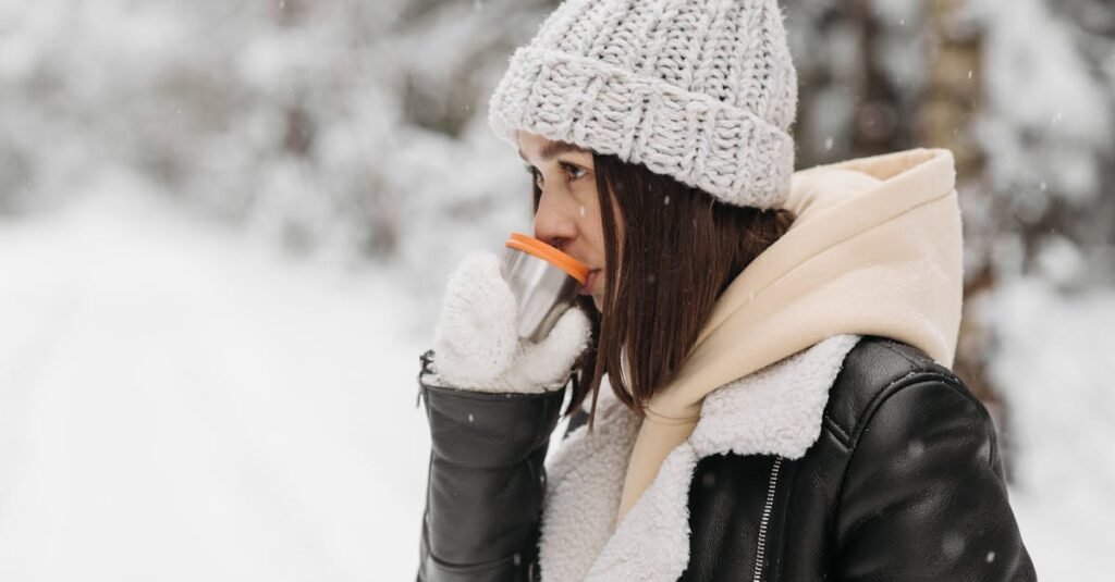 A woman in warm clothing enjoys a hot drink amidst a snowy winter landscape.