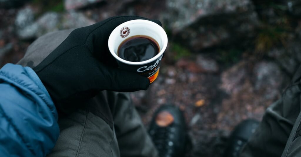 A gloved hand holding a disposable cup of coffee outdoors, perfect for camping vibes.